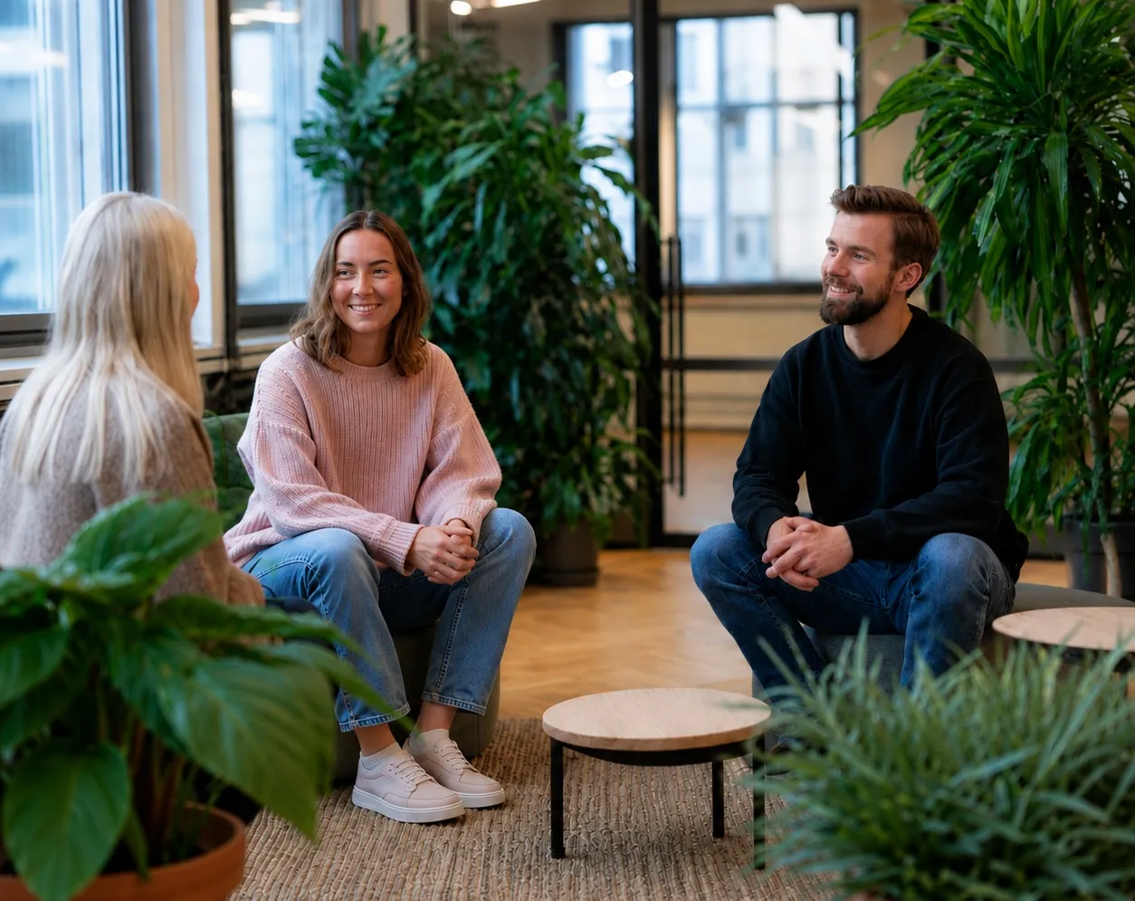 Kolme asiantuntijaa keskustelee rennossa toimistoympäristössä viherkasvien keskellä